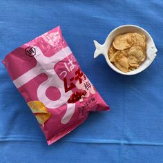 a bowl of chips next to a bag of potato chips on a blue tablecloth