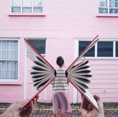 two hands holding up an open book in front of a pink building with white windows