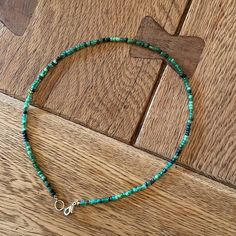 a turquoise beaded necklace on a wooden floor with a cross in the middle and a small silver charm hanging from it