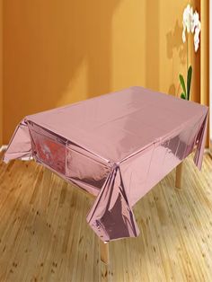 a shiny pink tablecloth on a wooden floor in front of an orange wall with white flowers