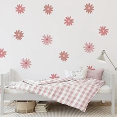 a white bed sitting under a pink flower wall decal next to a checkered blanket