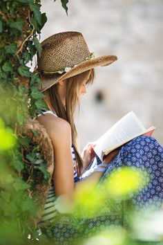 a woman sitting on the ground reading a book while wearing a straw hat and dress