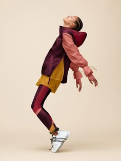 a woman in purple jacket and yellow pants doing a dance move with her arms outstretched