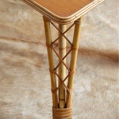 a small table made out of bamboo and wicker with a wooden top on a cowhide rug