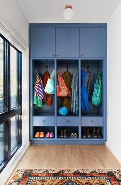 a blue closet with several coats and purses hanging on the doors, in front of a large window