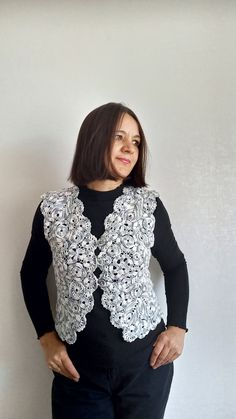 a woman standing in front of a wall wearing a black and white sweater with crochet on it