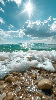 the sun shines brightly over an ocean beach with rocks and foamy water in the foreground