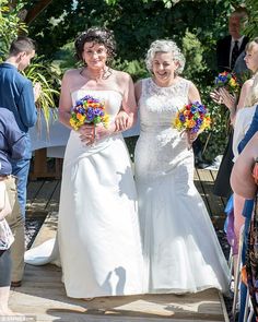 two women in white dresses are walking down the aisle