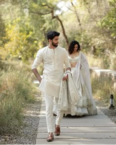 a man and woman walking down a path in the woods wearing white outfits with matching dupattas