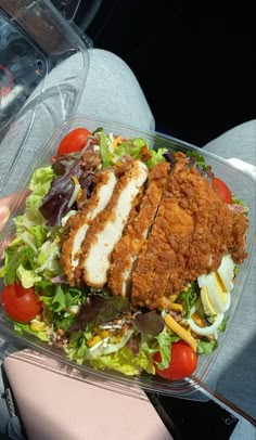 a person holding a plastic container filled with salad and chicken breast patties on top of lettuce