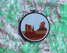 a map with some mountains in the background and a small embroidered ornament hanging on it