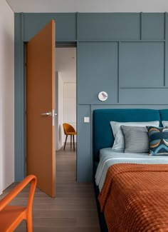 an orange and blue bed in a bedroom next to a wooden door with two chairs