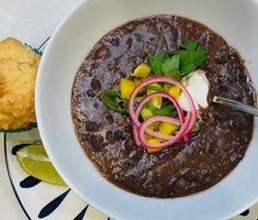 a white bowl filled with black bean soup next to a muffin on a blue and white plate