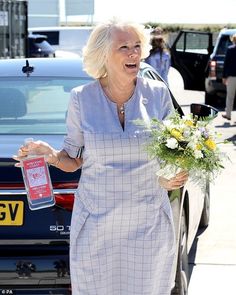 an older woman is walking with flowers in her hand and holding onto the handle of a car