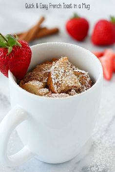 a cup filled with french toast and powdered sugar next to strawberries on a table