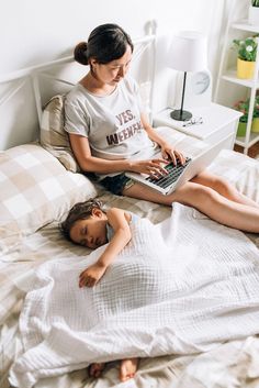 a woman sitting on top of a bed next to a child using a laptop computer