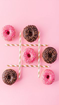 four donuts with pink glaze and chocolate sprinkles arranged on sticks