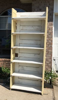 an old yellow shelf sitting in front of a brick building with white shutters on it