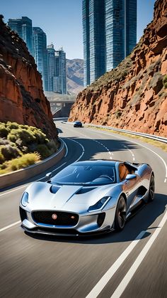 a silver sports car driving down the road in front of some tall buildings and mountains