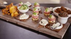 small appetizers are arranged on a cutting board with chips and dips in bowls