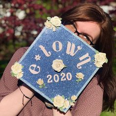 a woman holding up a blue graduation cap with flowers on it that says slow to go