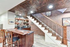 a bar with stools in front of a brick wall and stairs leading up to the second floor