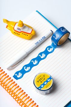 an open notebook with various items on it and a yellow toy boat next to it