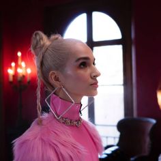 a woman with pink hair and earrings in a room next to a candlelight chandelier