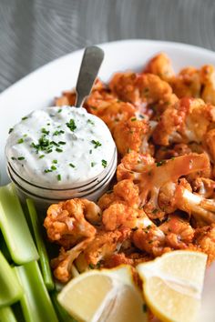 a white plate topped with cauliflower, celery and lemon wedges