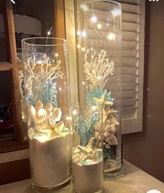 two glass vases filled with flowers and lights on top of a table next to a window