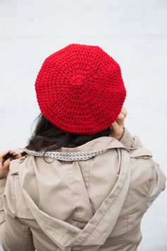 a woman wearing a red crochet hat while standing in front of water with her back to the camera