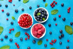 berries, raspberries and blueberries in small white bowls on a blue surface