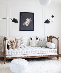 a white day bed with pillows on it in front of a wall and a painting