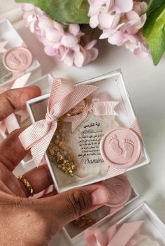 a person holding a small box with some pink items in it and flowers on the table