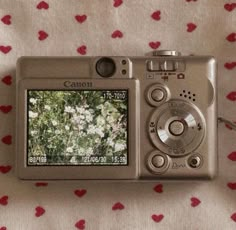 a digital camera sitting on top of a bed next to a red and white blanket