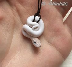 a hand holding a white necklace with a snake on it's end and black string