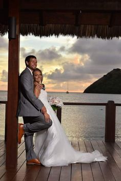 a bride and groom pose for a photo on the dock in front of an ocean