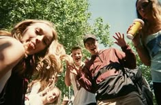 a group of young people standing next to each other in front of trees and bushes