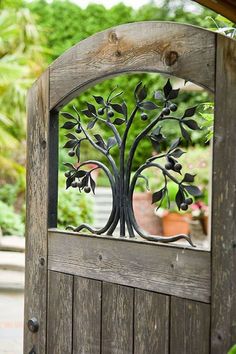 an open wooden door with a metal tree on the top and bottom part, in front of a garden