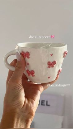 a hand holding a white cup with red bows on the inside and pink flowers on the outside