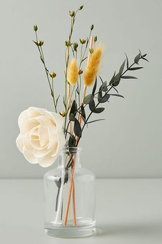 a glass vase filled with flowers on top of a white tablecloth covered floor next to a gray wall