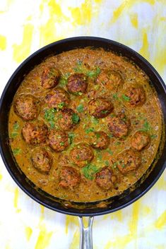 a skillet filled with meatballs and sauce on top of a yellow table cloth