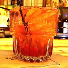 an orange drink sitting on top of a table next to a cup with straws in it