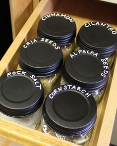 six jars filled with different kinds of food on top of a wooden drawer in a kitchen