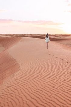 a woman walking in the desert at sunset