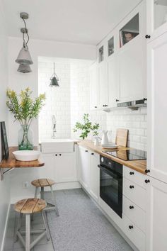 a small kitchen with white cabinets and wooden counter tops, along with two stools