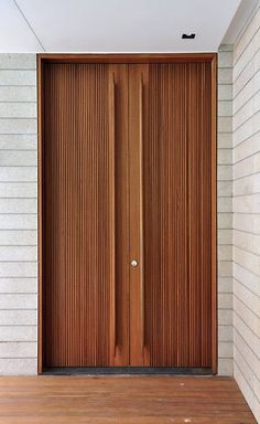 an open wooden door on the side of a white brick building with wood flooring