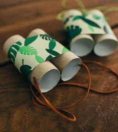 two rolls of toilet paper with green leaves on them sitting on a wooden table next to a string