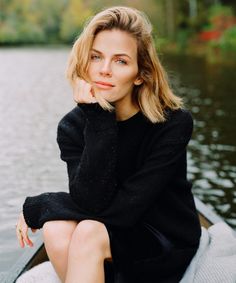 a woman sitting on top of a boat next to the water with her hand under her chin