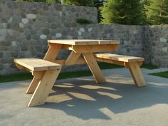 a wooden picnic table sitting in the middle of a cement area next to a stone wall